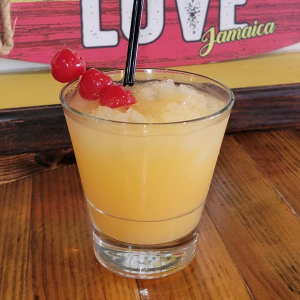 A Caribbean cocktail with crushed ice, garnished with three red cherries and a black straw.