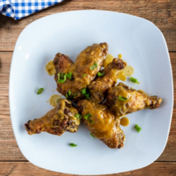 Five Caribbean jerk chicken wings with sauce and green onions on a white plate.
